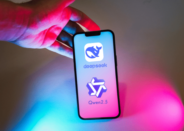 Un téléphone avec les logos d'applications d'IA chinoises DeepSeek et Qwen affichés sur l'écran. Une main le maintient debout au-dessus, et le tout est éclairé par des couleurs néon rose et bleue.